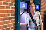 Pretty happy student withdrawing cash smiling at camera at an ATM