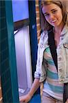 Pretty cheerful student withdrawing cash smiling at camera at an ATM