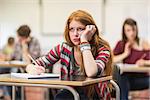 Bored young female student with others writing notes in the classroom