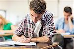 Young male student with others writing notes in the classroom