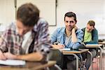 Portrait of a smiling male student with others writing notes in the classroom