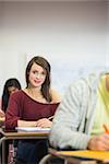 Portrait of a smiling female student with others writing notes in the classroom