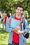 Portrait of college boy holding books with blurred students standing in the park