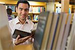 Close up portrait of a smiling mature student with book by shelf in the library