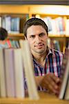 Close up of a smiling mature student selecting book from shelf in the library