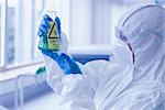 Close up side view of a scientist in protective suit looking at hazardous blue chemical in flask at the laboratory