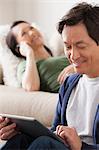 Mature man using digital tablet, woman lying on sofa