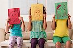 Three girls holding pictures over faces