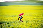 Young woman running in oil seed rape field with red umbrella