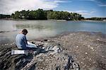 Mature man sitting on rocks looking at maps, Bath, Maine, USA