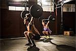 Two young adults lifting barbells in gym