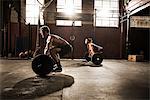 Two young adults working out with barbells in gym