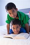 Brothers looking up from book on bed