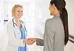 Doctor and businesswoman handshaking in hospital corridor