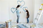 Mother and daughter painting blue hearts on wall in new house