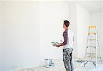 Man with paint tray looking up at white wall