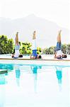 Men and woman practicing yoga poolside