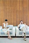 Couple using laptop and cell phone in armchairs