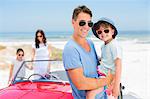 Father and son smiling near convertible on beach