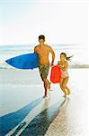 Father and daughter carrying surfboard and bodyboard on beach