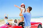 Father lifting daughter from convertible at beach