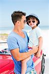 Father and son smiling on beach next to convertible