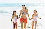 Mother and daughters holding hands and running on beach