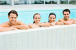 Portrait of smiling friends leaning at edge of swimming pool