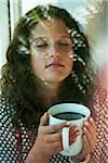 Teenage girl sitting next to window, holding cup in hands, Germany