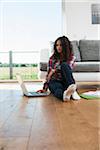 Teenage girl sitting on floor next to sofa, using laptop computer, Germany