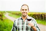 Portrait of vintner standing in vineyard, holding glass of wine, smiling and looking at camera, Rhineland-Palatinate, Germany