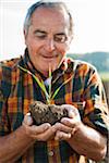 Close-up portrait of farmer standing in field, holding seedling plant from crop, Germany