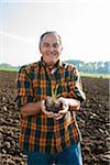 Portrait of farmer standing in field, holding seedling plant from crop, Germany