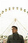 Portrait of young man standing in front of ferris wheel at amusement park, Germany