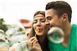 Close-up portrait of young couple blowing bubbles at amusement park, GermanyYoung