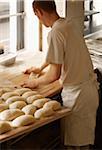 Male baker shaping baguette bread dough by hand in bakery, Le Boulanger des Invalides, Paris, France