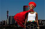 Traditionally dressed African woman stands with cityscape in background