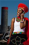 Traditionally dressed African woman talks on cellphone with cityscape in background