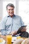 Smiling mature man with digital tablet at breakfast