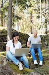 Couple in forest using laptops, Sweden