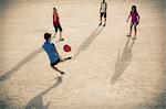 Children playing with soccer ball in sand