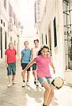 Boys watching girl play with soccer ball in alley