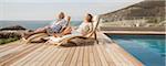 Older couple relaxing in lawn chairs by pool