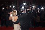 Rear view of well dressed couple waving to paparazzi at red carpet event