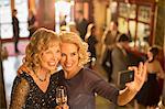 Well dressed women with champagne taking self-portrait with camera phone in theater lobby