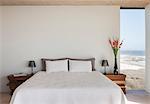 Vase of flowers next to bed in bedroom with ocean view