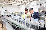 Supervisor and manager watching plastic bottles on conveyor belt