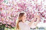 Woman taking self-portrait under tree with pink blossoms