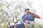 Man lifting woman under tree with white blossoms