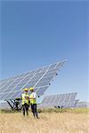 Workers standing by solar panels in rural landscape